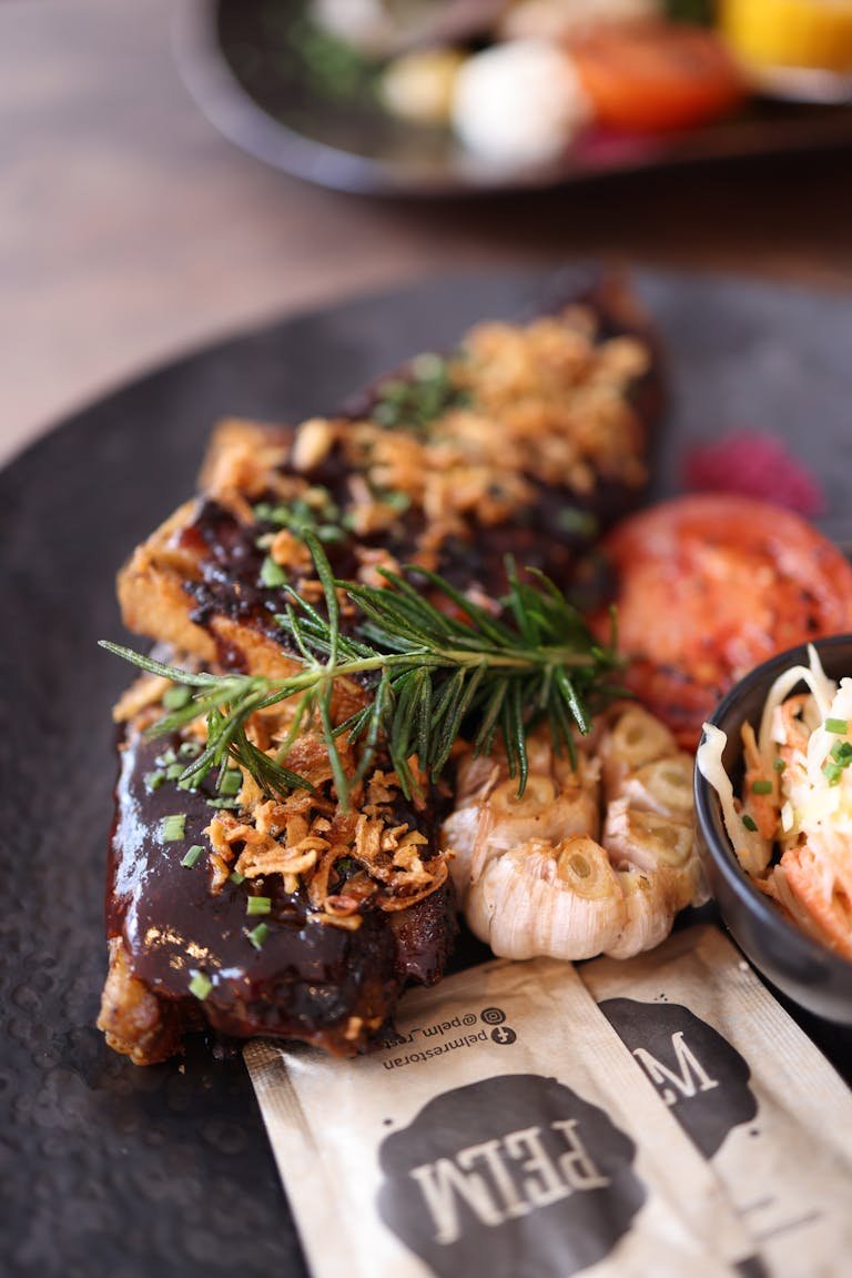 A gourmet steak dish beautifully garnished with rosemary and fried onions, served on a black plate.