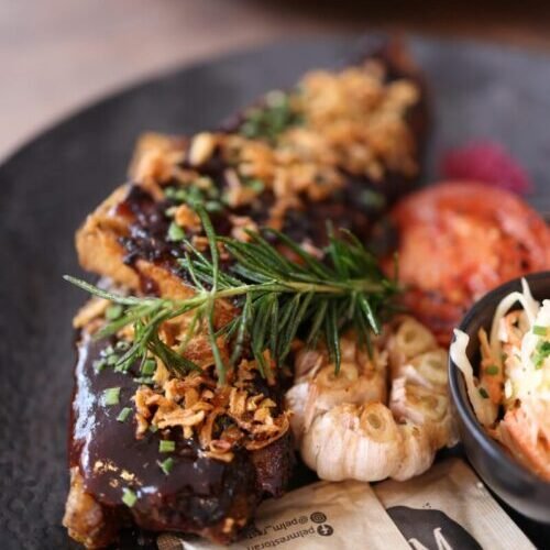 A gourmet steak dish beautifully garnished with rosemary and fried onions, served on a black plate.