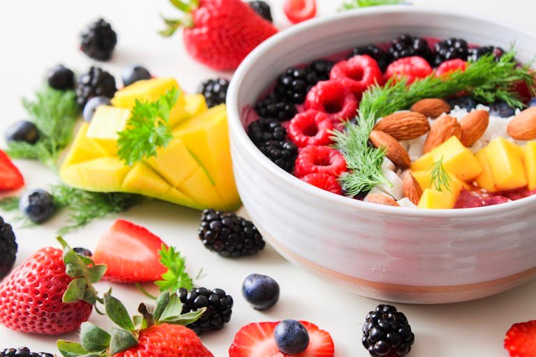 A vibrant bowl filled with fresh berries, mango, almonds, and herbs, perfect for a healthy snack or breakfast.