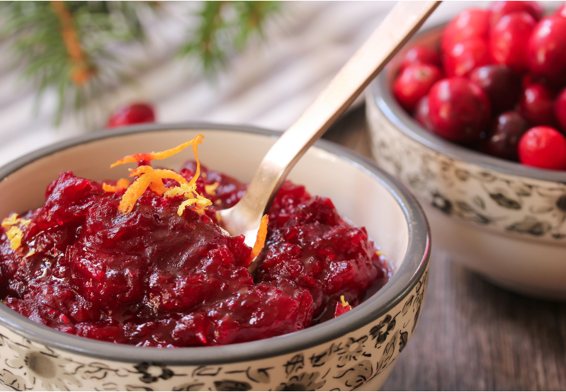Cranberry sauces in a bowl with cranberries in a seperate bowl behind it