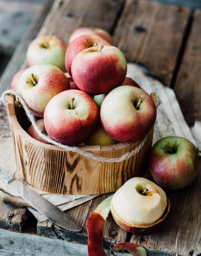 A close-up of ripe apples in a wooden basket on rustic planks. Ideal for fall harvest themes.