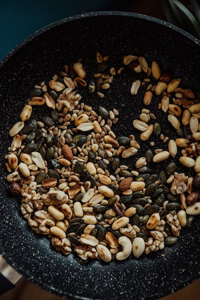 Close-up of assorted nuts and seeds roasting in a frying pan, ideal for vegan cooking.