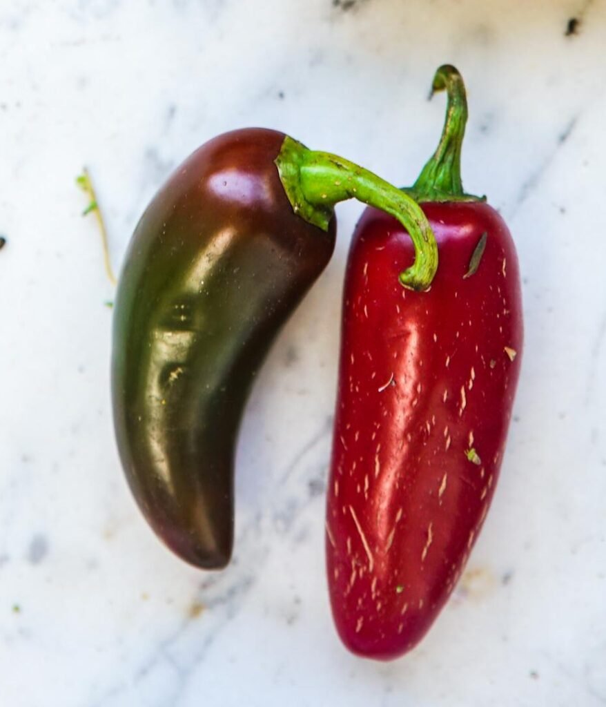 Close-up of vibrant jalapeño peppers spilling from a paper bag on a marble surface, perfect for spicy food concepts.