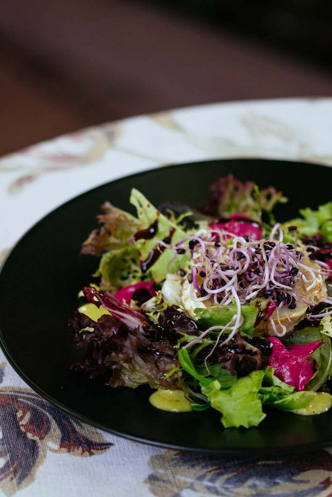 A fresh and colorful mixed green salad garnished with microgreens and dressing. black garlic salad dressings