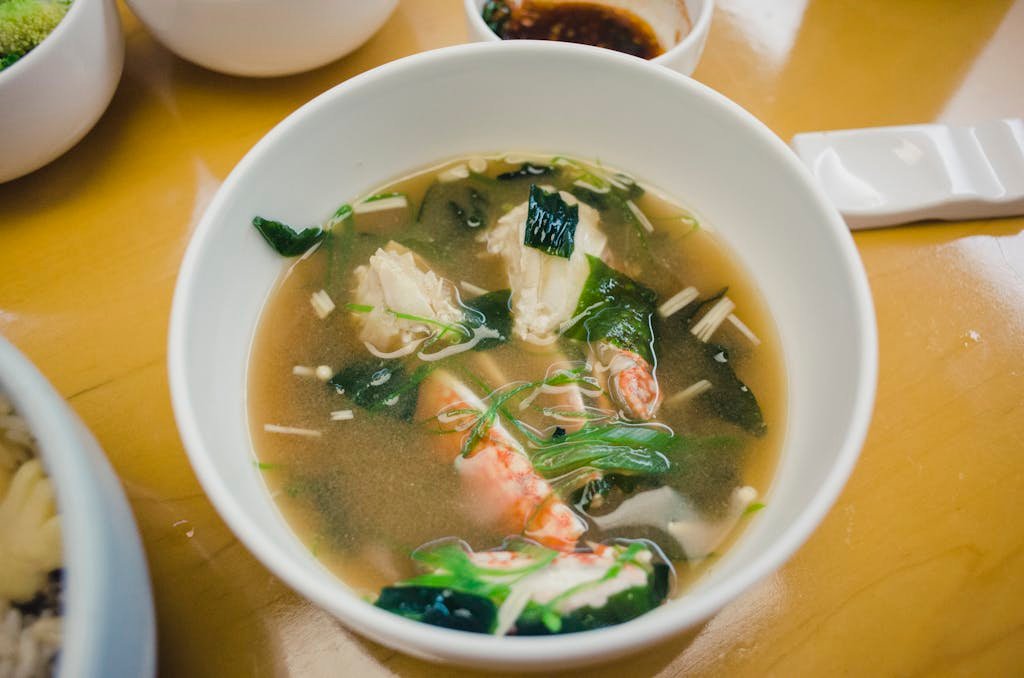 Close-up of a bowl of Japanese miso soup with seafood, tofu, and fresh greens, showcasing its delicious and healthy appearance.