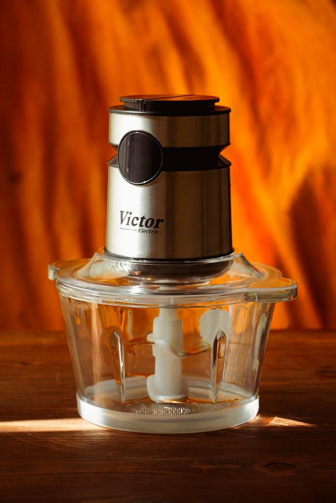 Stainless steel food processor with glass bowl and blades against a warm backdrop.
