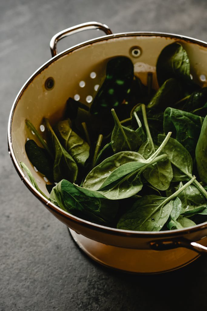 A colander filled with fresh, washed organic spinach leaves in a kitchen setting.