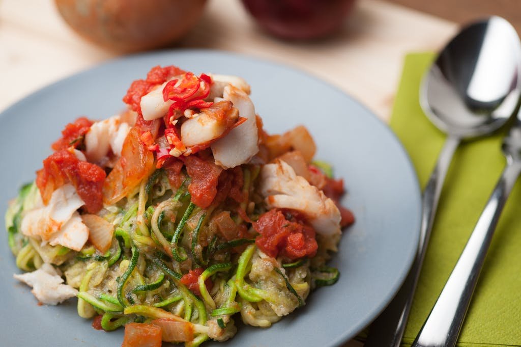 A plate of Black Garlic Spinach and chicken Zoodles topped with fresh tomato and fish, ideal for a healthy keto meal.