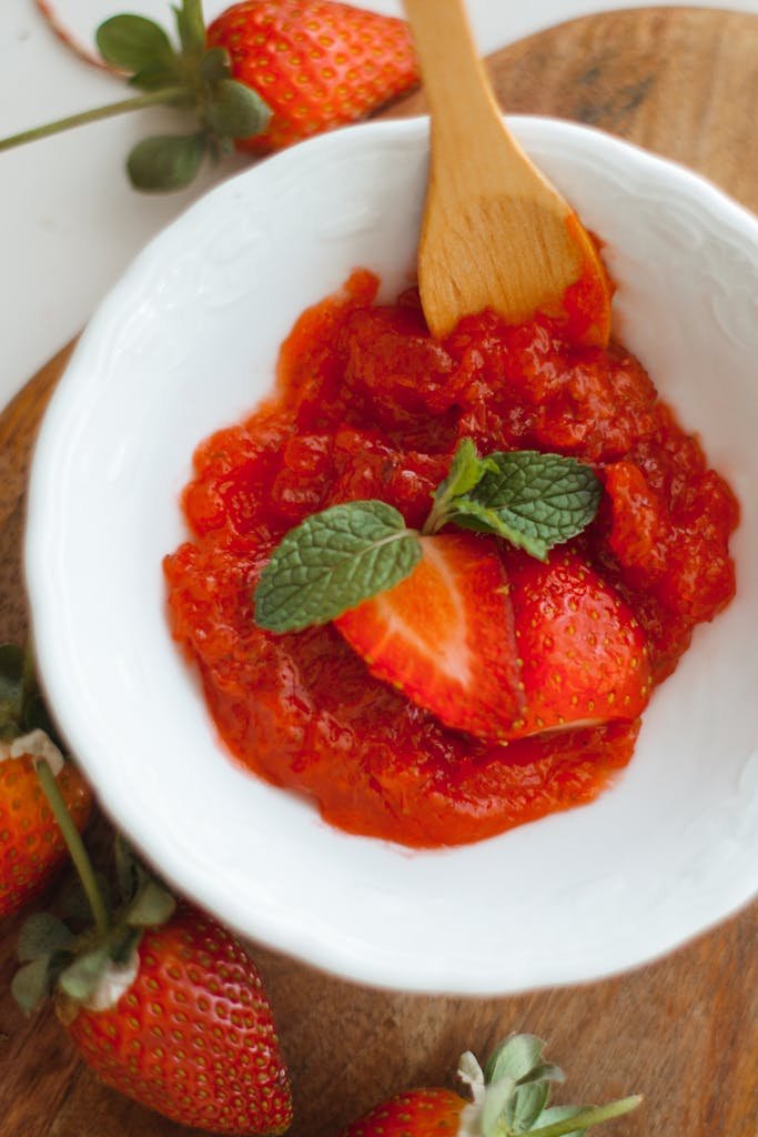 Close-up of fresh strawberry jam in a white bowl adorned with mint leaves.