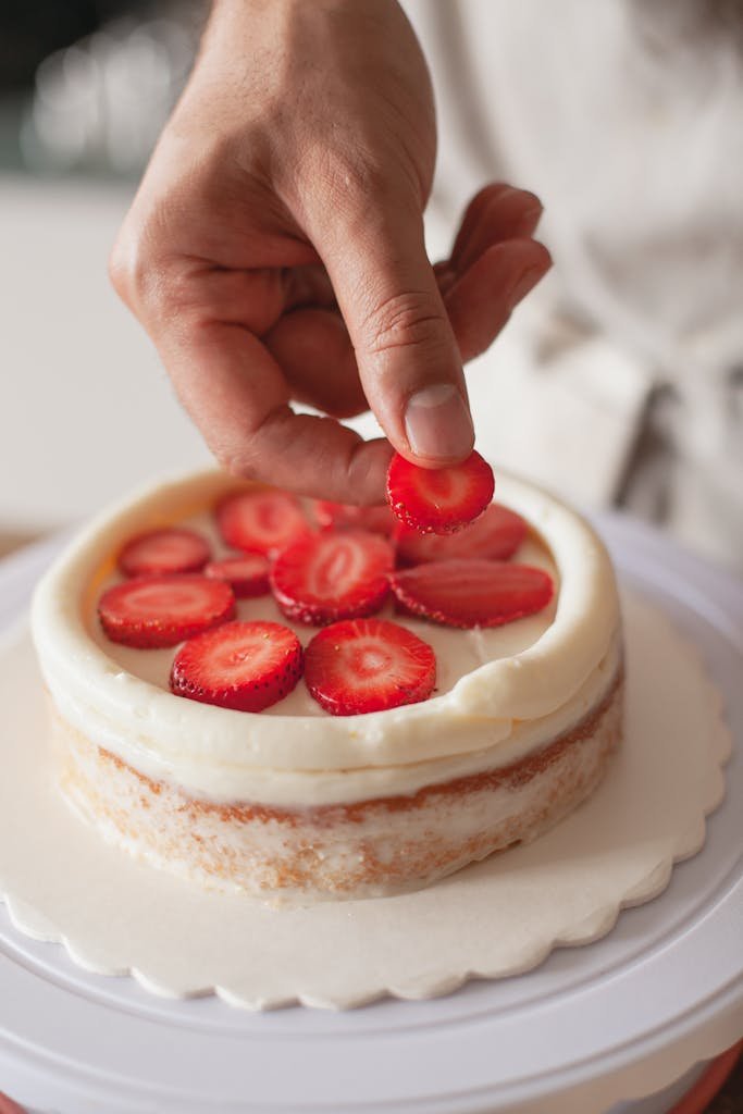 Close-up of hand decorating a cake with fresh strawberries, highlighting the art of cake design.