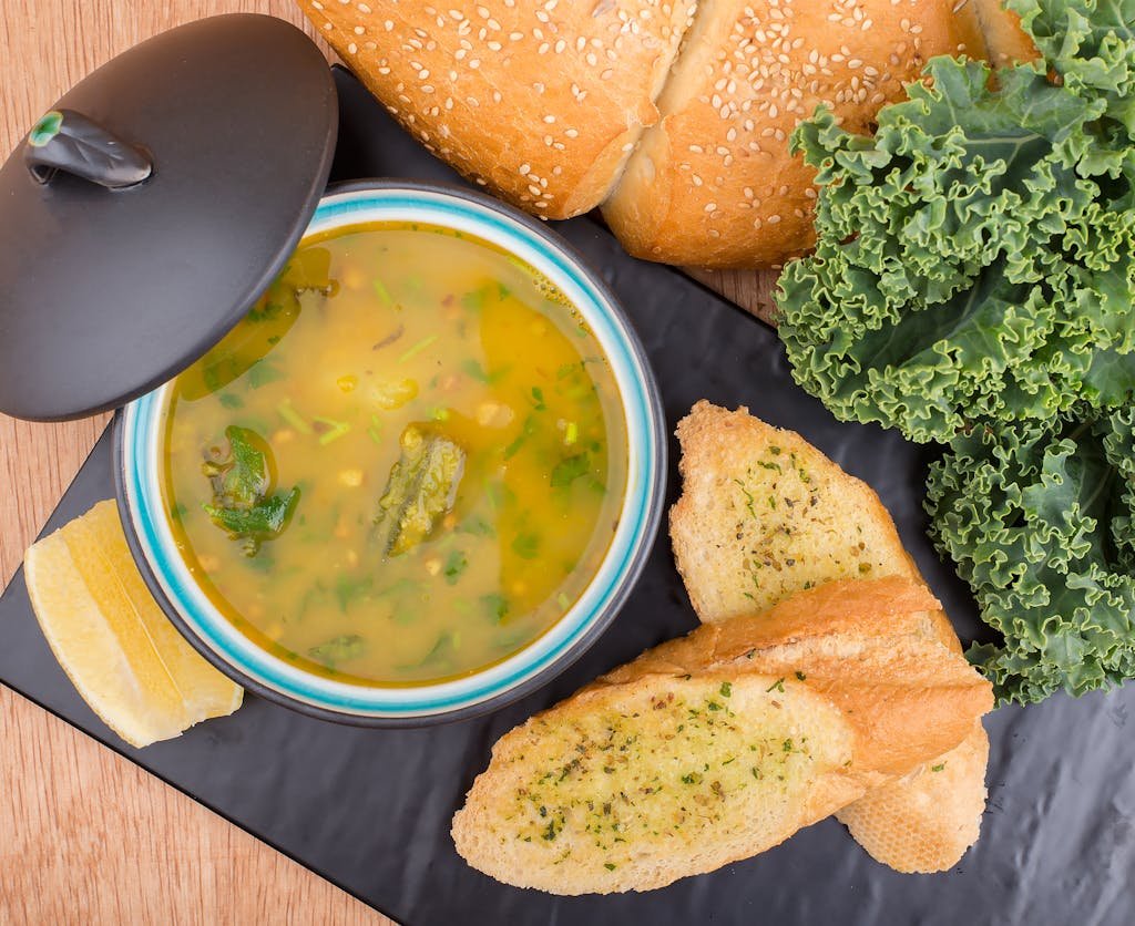 Delicious soup served with garlic bread, kale, white bean and foraged greens soup recipe and fresh loaf on a table.