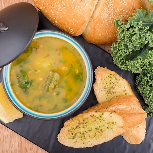 Delicious soup served with garlic bread, kale, white bean and foraged greens soup recipe and fresh loaf on a table.