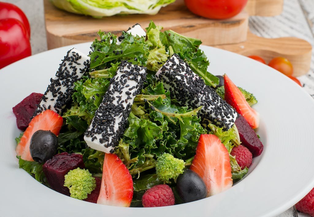 Fresh mixed green salad topped with black sesame cheese and colorful fruits, perfect for a healthy meal. kale and strawberry salad