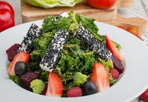 Fresh mixed green salad topped with black sesame cheese and colorful fruits, perfect for a healthy meal. kale and strawberry salad
