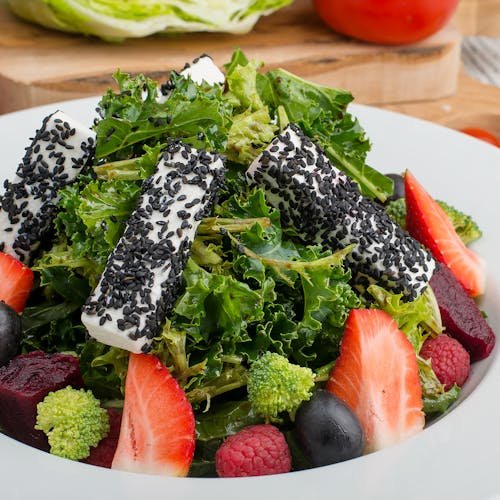 Fresh mixed green salad topped with black sesame cheese and colorful fruits, perfect for a healthy meal. kale and strawberry salad