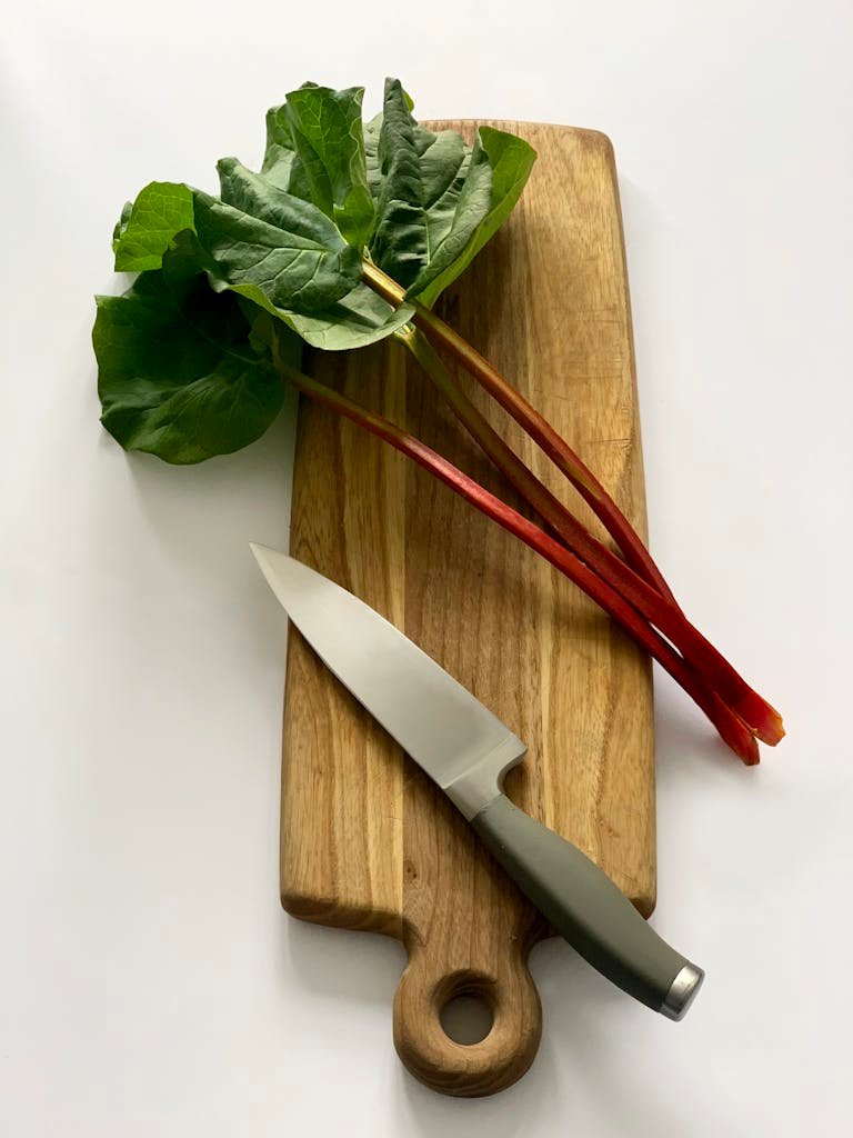 Top-down view of fresh rhubarb and knife on a wooden cutting board. Ideal for culinary themes.