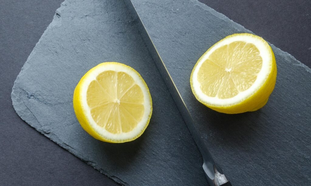 Close-up of lemon halves with knife on slate board, highlighting freshness and vibrant colors.