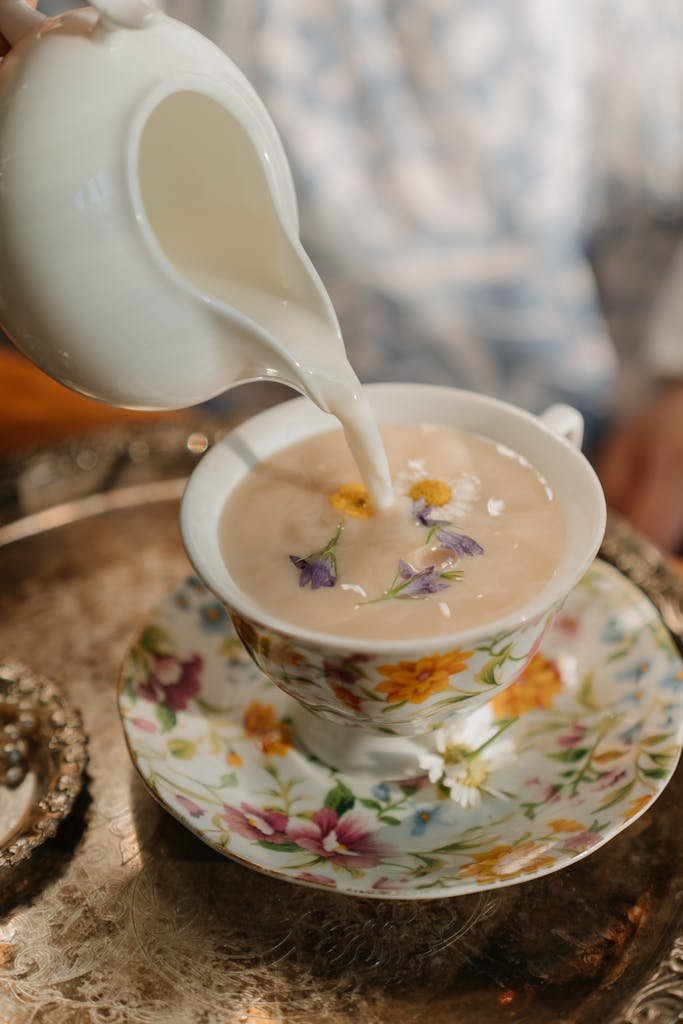 Pouring milk into a beautifully decorated floral porcelain teacup.
