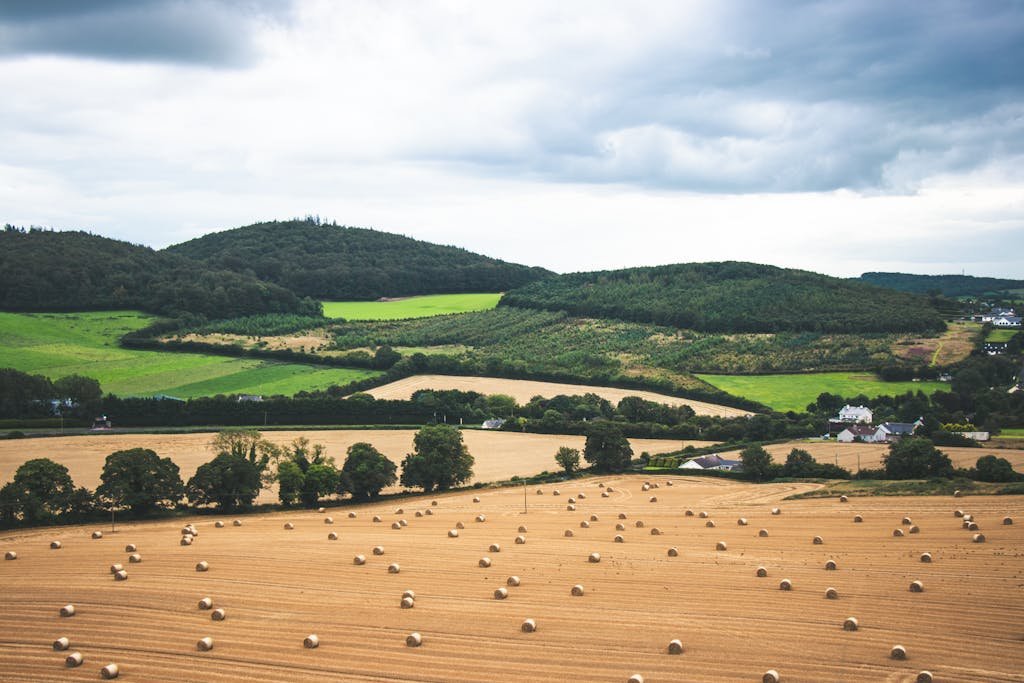 Wide view of a lush Irish landscape featuring hay bales and green rolling hills under a cloudy sky.