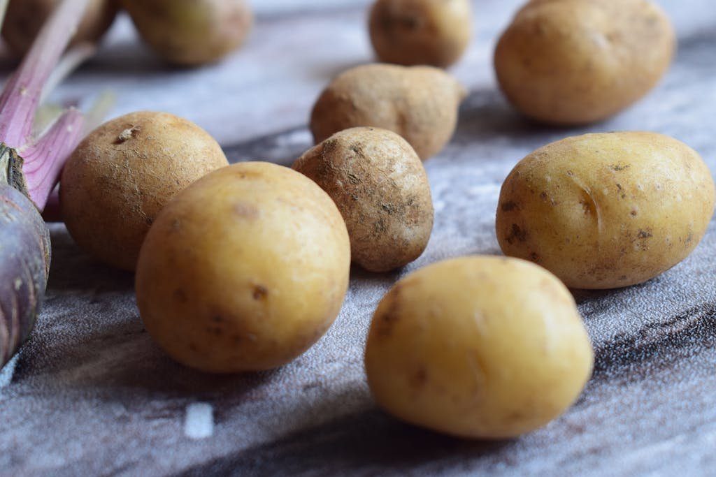 A close-up view of fresh, unpeeled potatoes scattered on a rustic wooden surface, highlighting their natural texture.