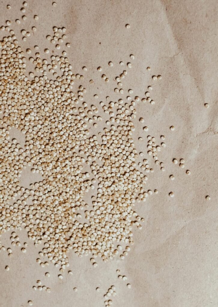 Overhead view of scattered organic quinoa seeds on textured brown paper background.