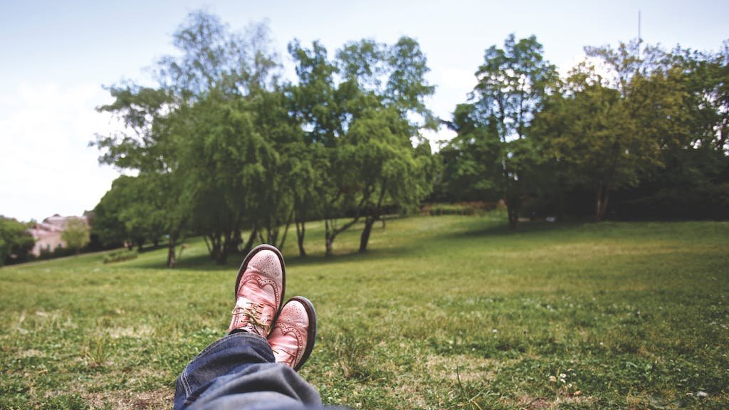 A person relaxes in a lush green park, feet up, enjoying a sunny day.