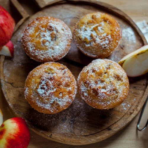 Top view of delicious baked muffins with powdered sugar placed near cut healthy apples in kitchen