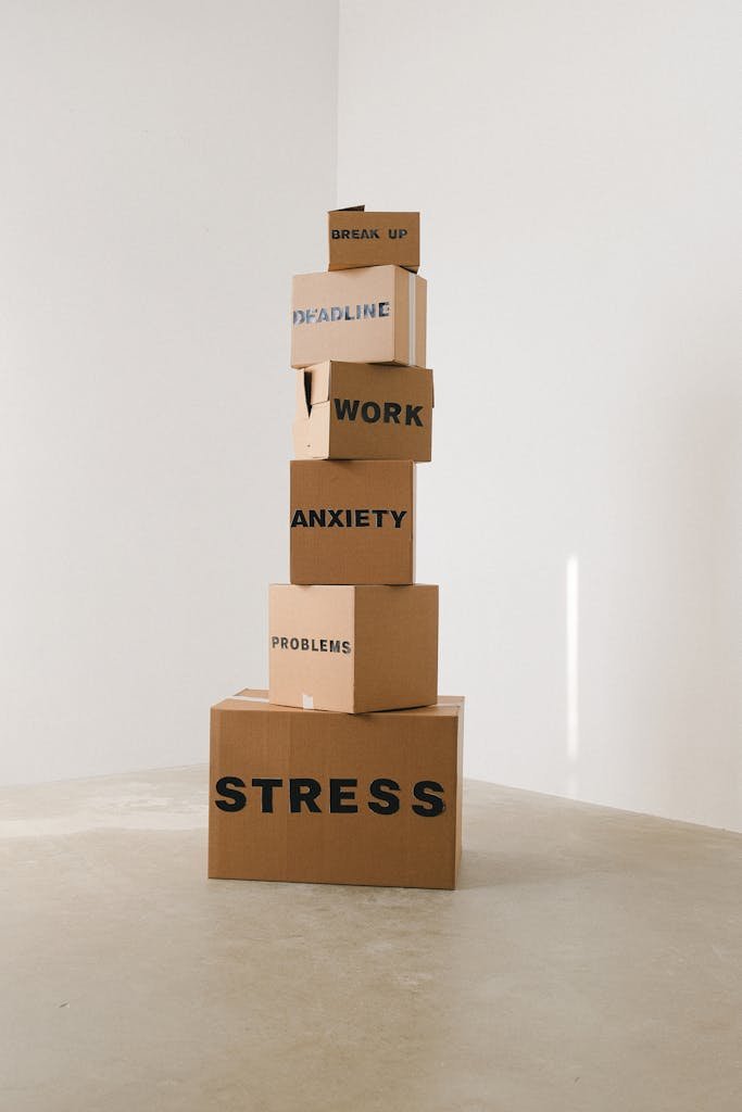 Vertical stack of cardboard boxes labeled with stress-related words, emphasizing mental health challenges.