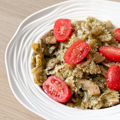 Tasty pesto pasta topped with cherry tomatoes on a white plate in a bright setting.